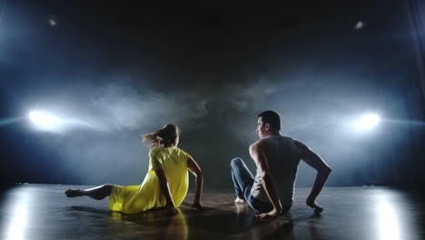 A-man-and-a-woman-dance-together-a-funny-dance-in-jeans-and-a-yellow-dress-on-stage-in-smoke.-Musical.
